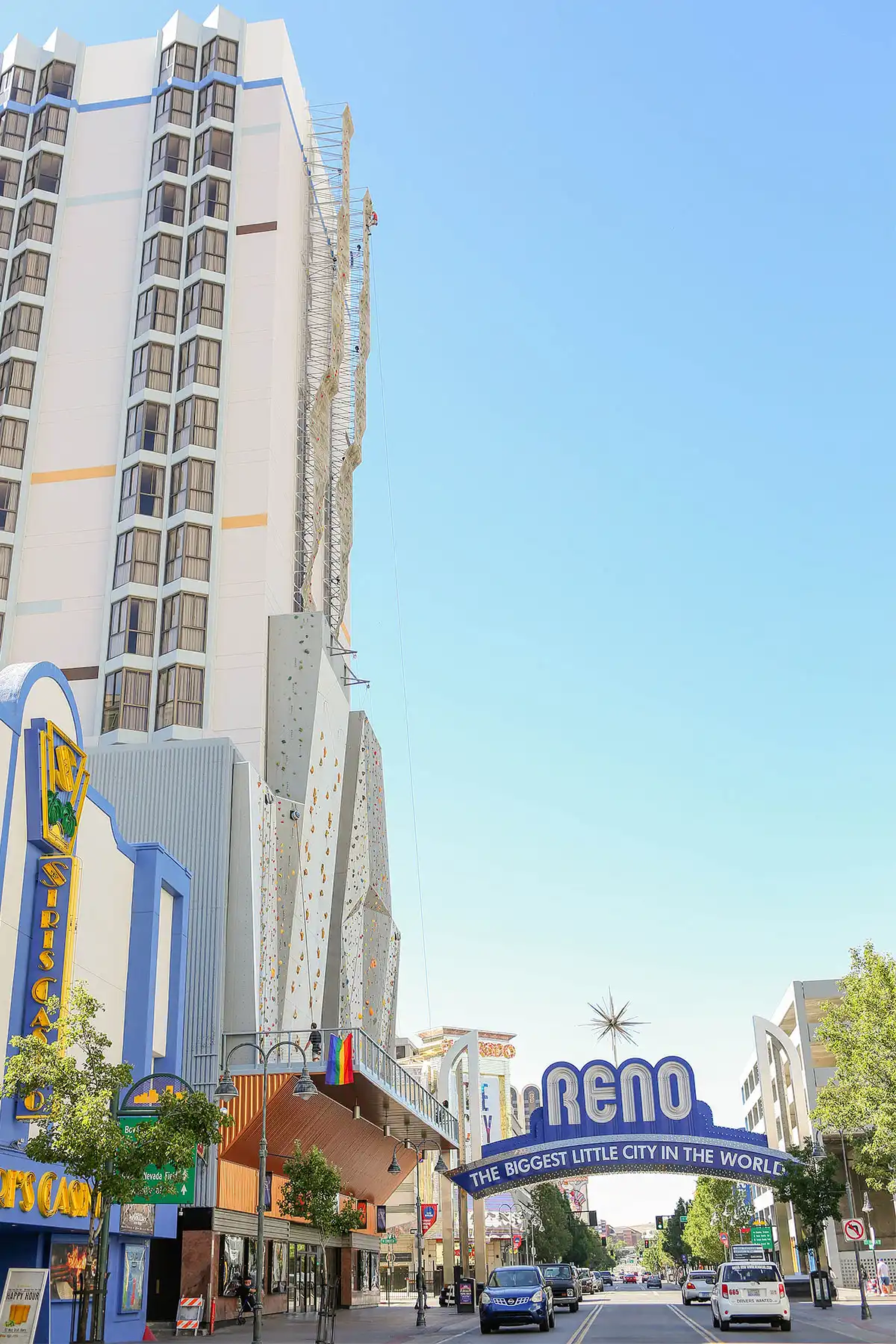 Sunny day with tiny person climbing outdoors on the worlds tallest climbing wall at Basecamp Climbing in Reno Nevada next to the street view of Reno Arch for scale
